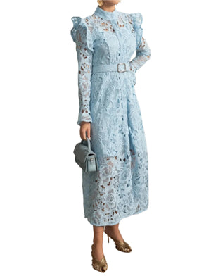 Woman in a light blue floral dress standing in a stylish room with decor elements.