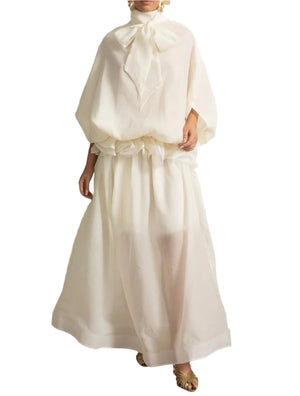 Woman wearing a white dress with a large bow in an elegant room.