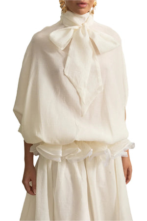 Person wearing a white outfit with a large bow in an elegant interior setting