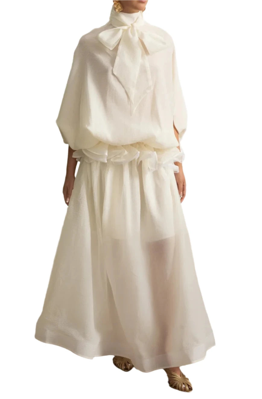 Woman wearing a white outfit with a large bow in an elegant room.