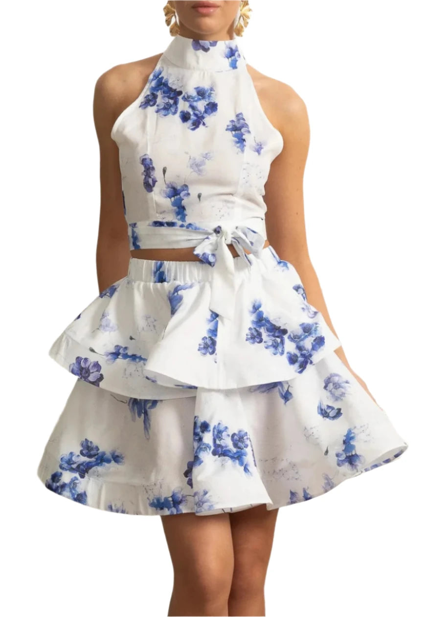 Woman wearing a white dress with blue floral patterns in an elegant indoor setting.