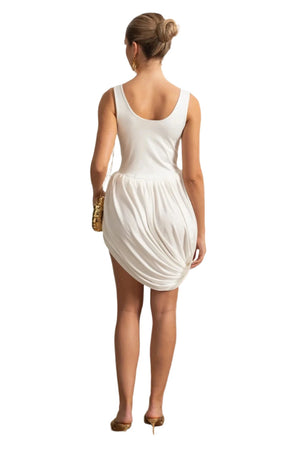 Woman in a white dress standing in a room with decorative wall molding and a plant.