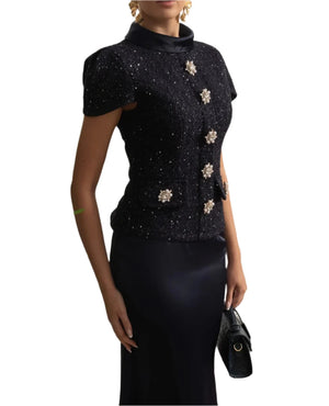 Woman wearing a black outfit with floral embellishments in an elegant interior setting.