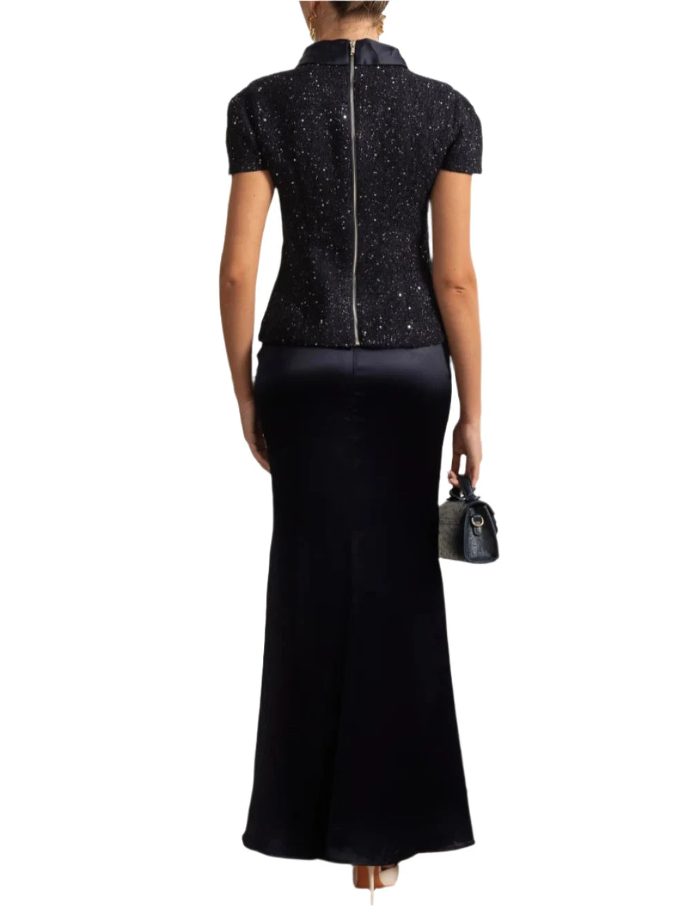Woman in a black dress standing in a room with decorative wall and plant.