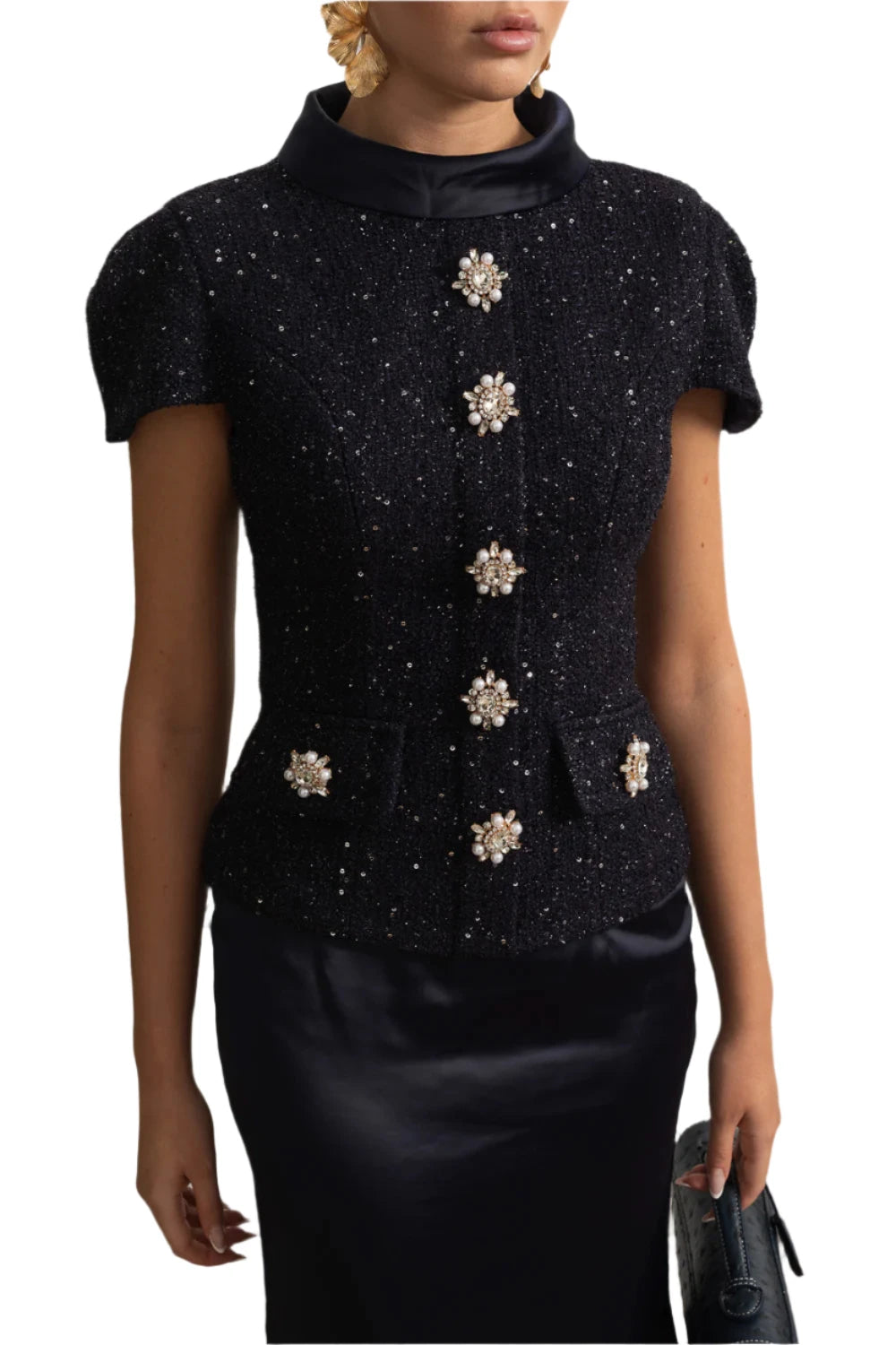 Black top with floral embellishments worn by a person against a decorative wall.