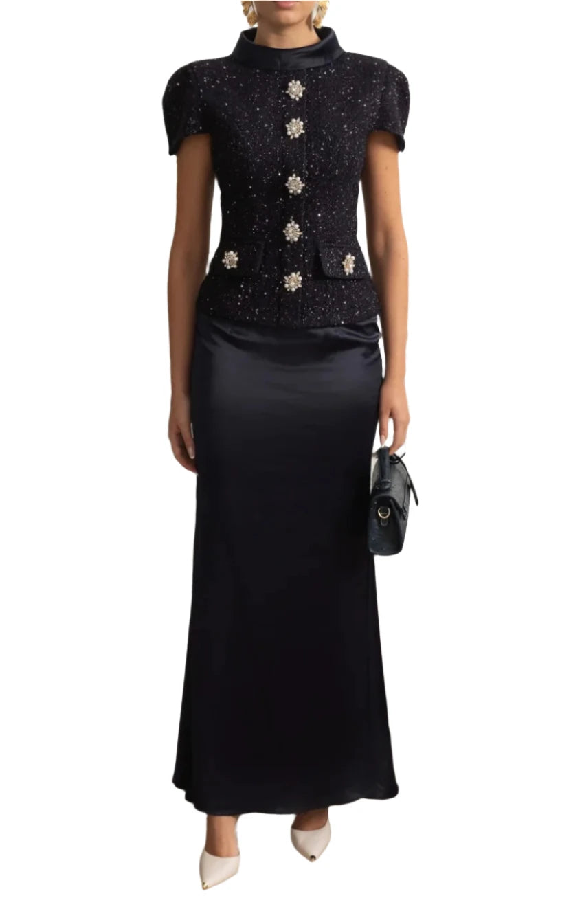 Woman in a black outfit with silver embellishments standing in a stylish room.