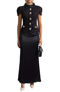 Woman in a black outfit with silver embellishments standing in a stylish room.