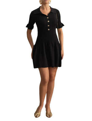 Woman wearing a black dress standing in a room with decorative wall and plant.