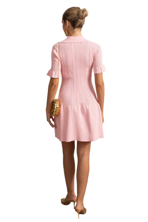 Woman wearing a pink dress standing in a room with decorative elements.